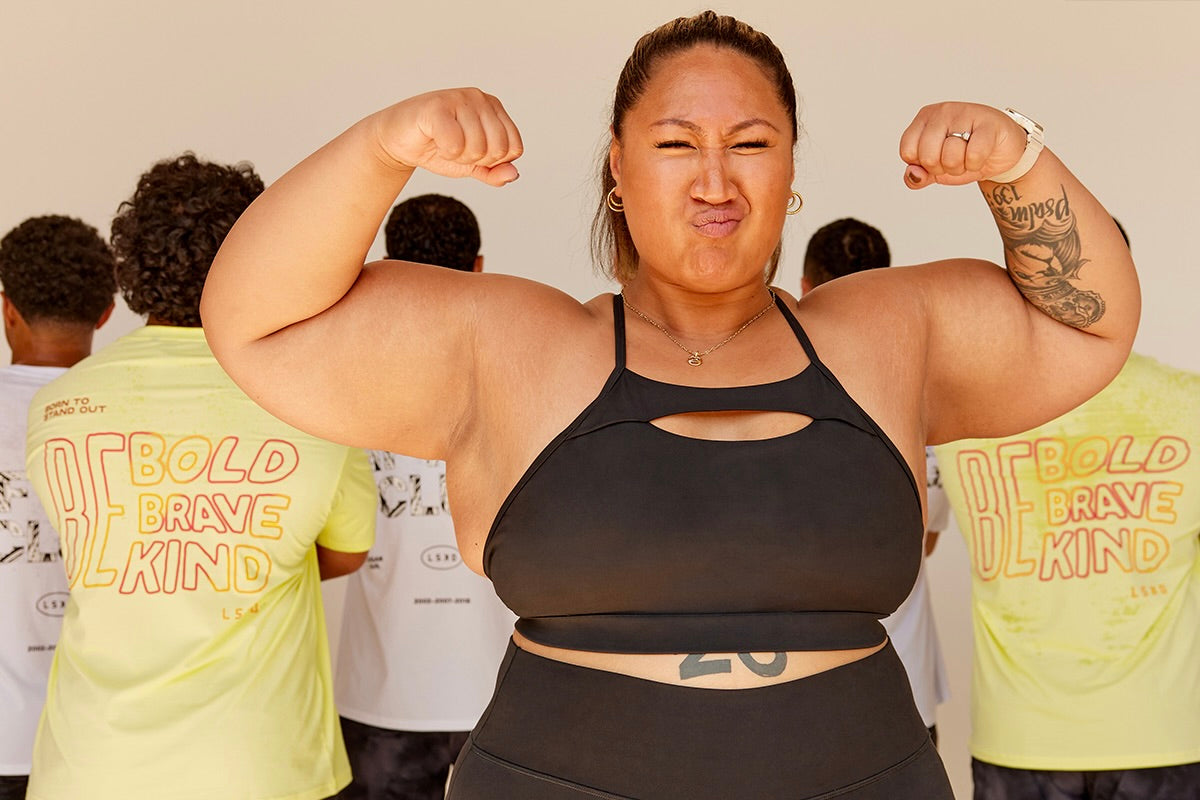 Woman flexing muscles in a black top, with others in the background.