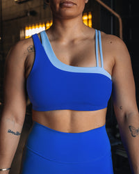 Woman wearing Thrive Asymmetric Sports Bra - Power Cobalt-Open Air | Model:Tiare | Size:M