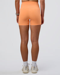 Woman wearing Fusion Ultra High-Rise 4" Short Pockets - Cantaloupe | Set:true | Angle:back | Model:Emelia | Size:S