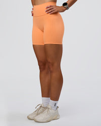 Woman wearing Fusion Ultra High-Rise 6" Short Pockets - Cantaloupe | Set:true | Angle:side | Model:Emelia | Size:S