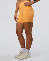 Woman wearing Fusion Ultra High-Rise 6" Short Pockets - Warm Apricot | Set:true | Angle:side | Model:Emelia | Size:S