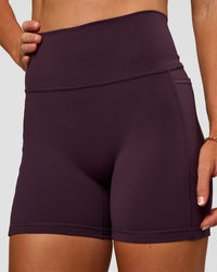 Woman wearing Fusion V-Contour Ultra High-Rise 4” Short Pockets - Midnight Plum | Model:Emelia | Size:S