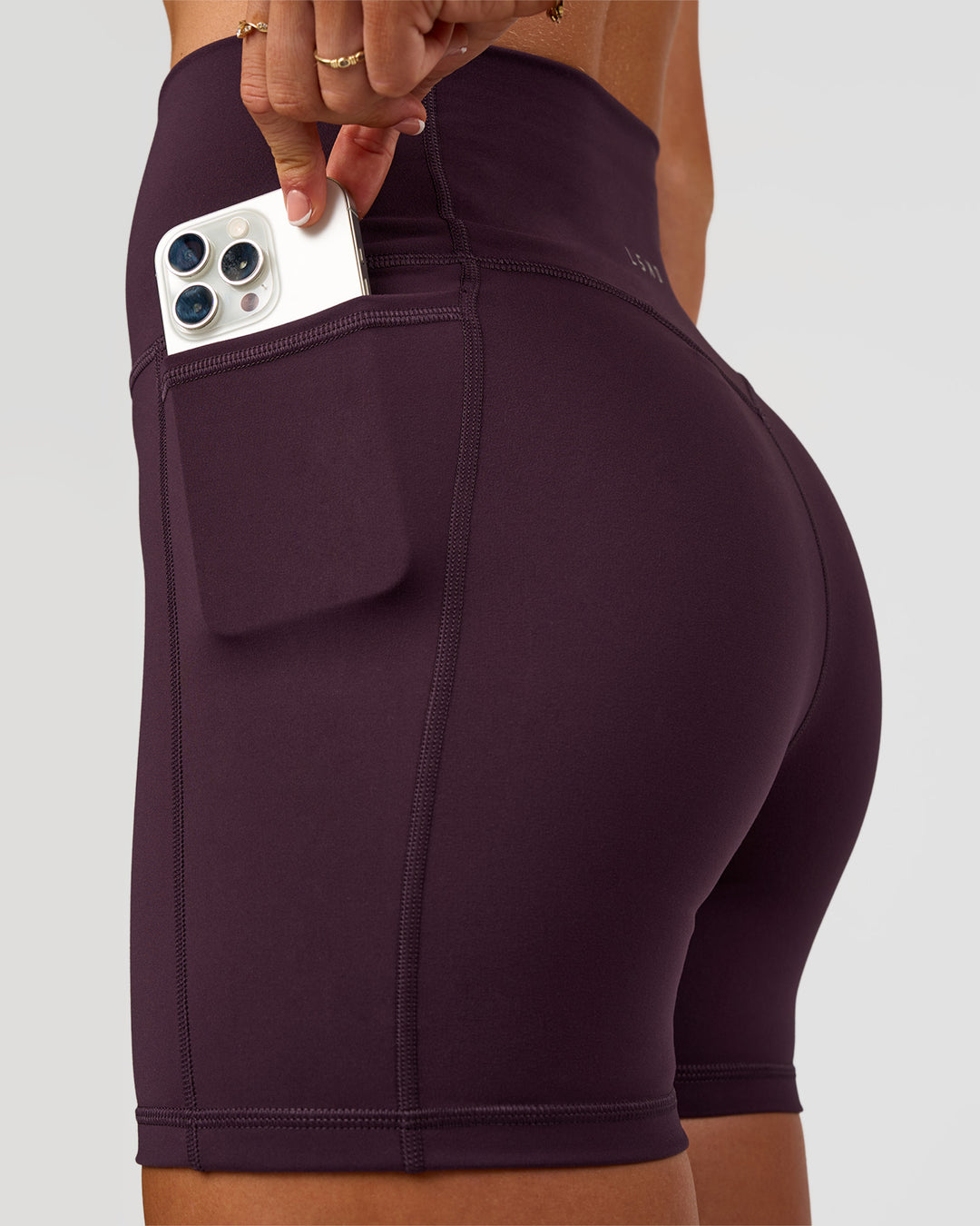 Woman wearing Fusion V-Contour Ultra High-Rise 4” Short Pockets - Midnight Plum | Model:Emelia | Size:S