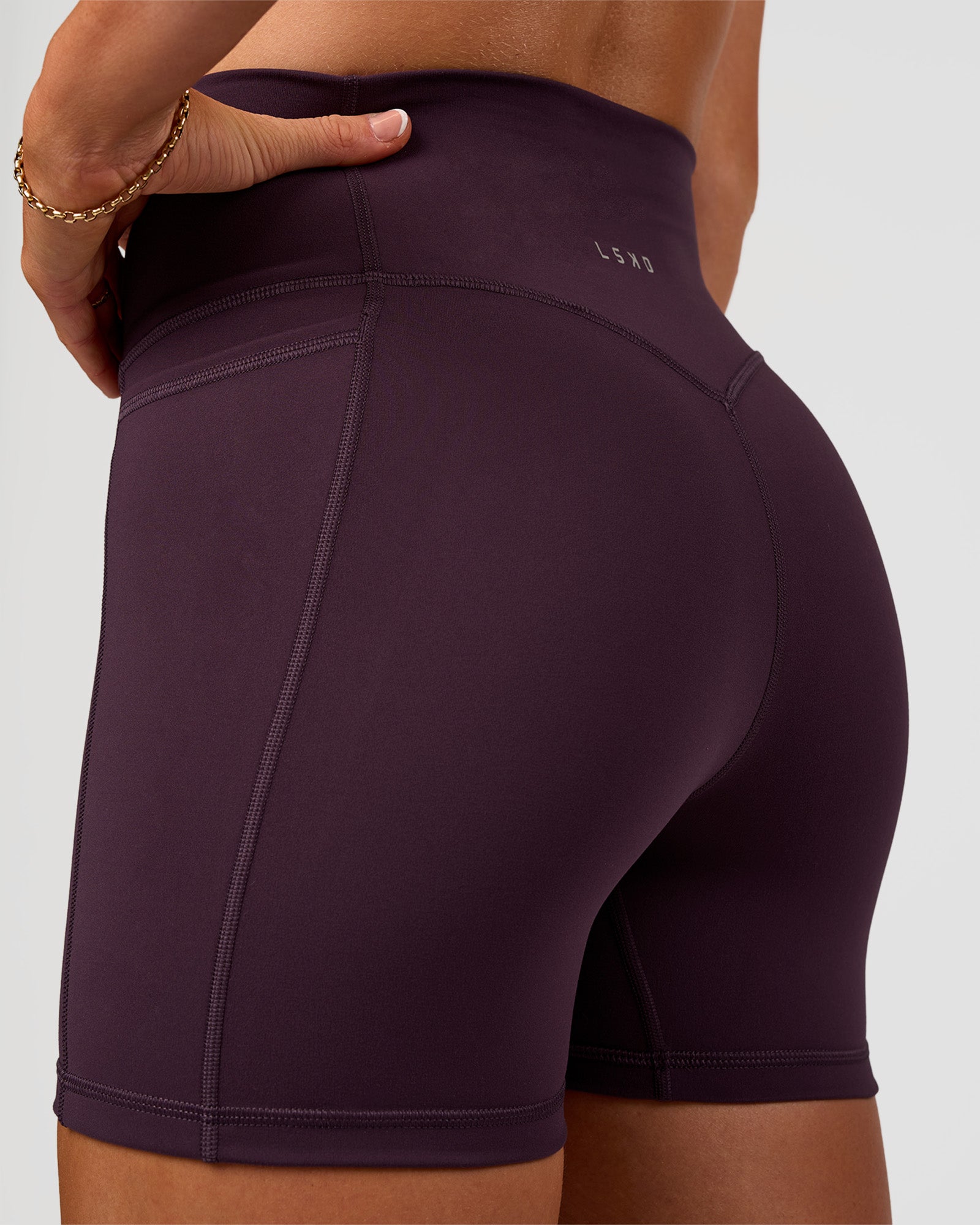 Woman wearing Fusion V-Contour Ultra High-Rise 4” Short Pockets - Midnight Plum | Model:Emelia | Size:S