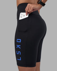 Woman wearing Rep Ultra High-Rise 9" Short Pockets - Black-Power Cobalt | Model:Rhiley | Size:S