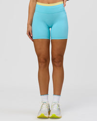 Woman wearing Lume Fusion Mid-Rise V Contour 6" Short Pockets - Baltic Sea-Lemon | Model:Grace | Size:XS