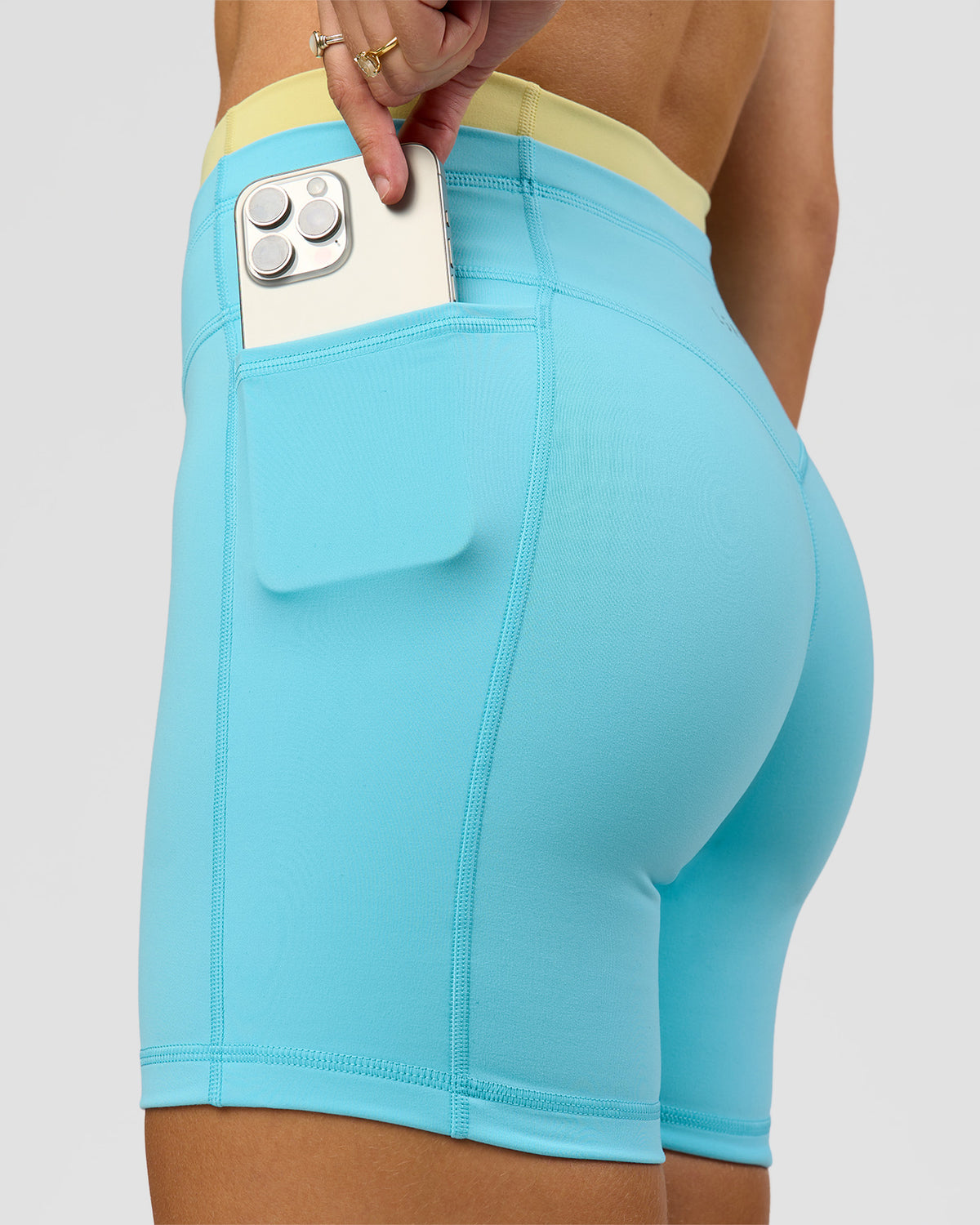 Woman wearing Lume Fusion Mid-Rise V Contour 6" Short Pockets - Baltic Sea-Lemon | Model:Grace | Size:XS
